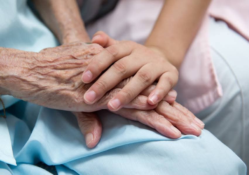 Caregiver's hand resting gently on an elderly patient's hands — compassionate care in Centurion